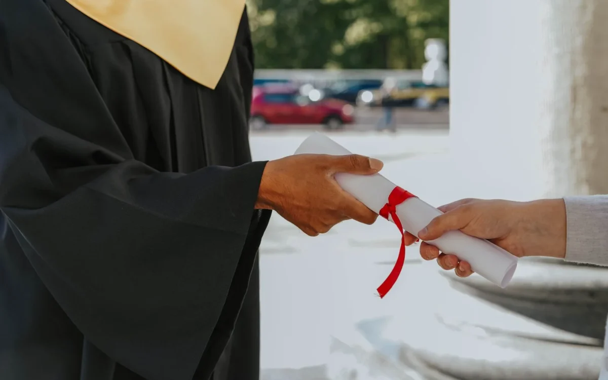 O persoană în robă de absolvire primește o diplomă la o ceremonie.