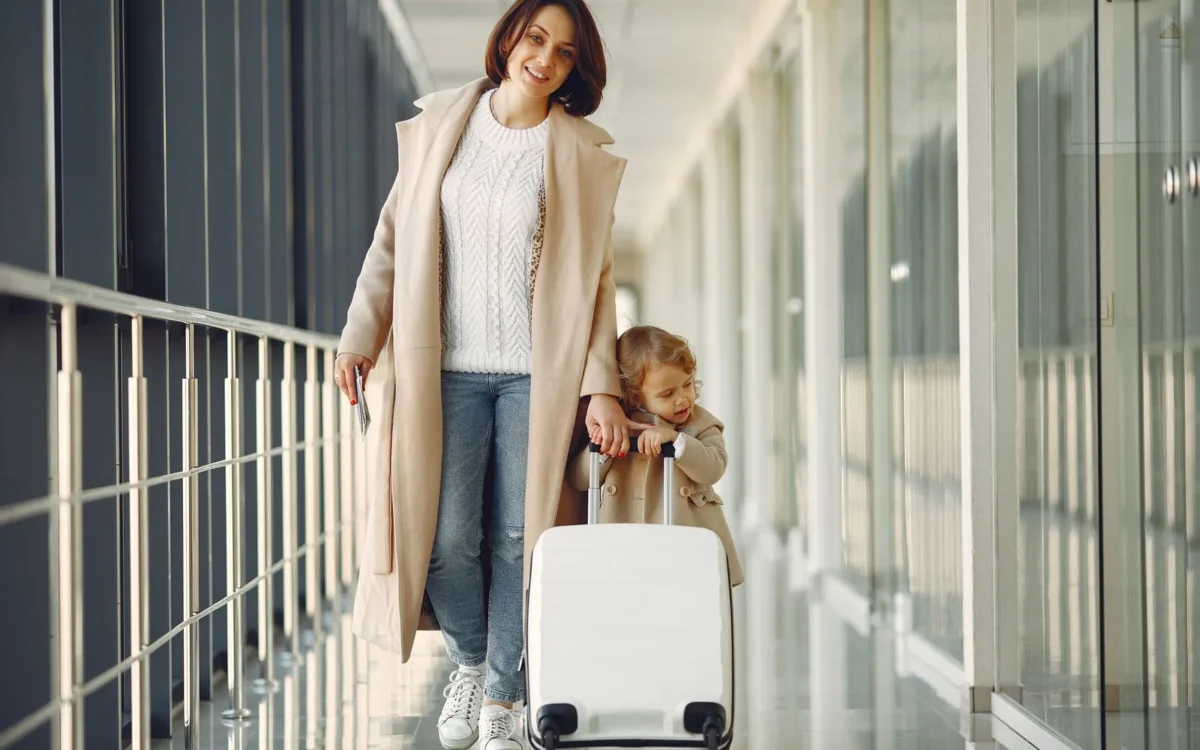 O femeie și un copil stau cu o valiză într-un terminal de aeroport.