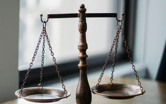 Balanță metalică și ciocan judecătoresc pe un birou, în fața unei ferestre