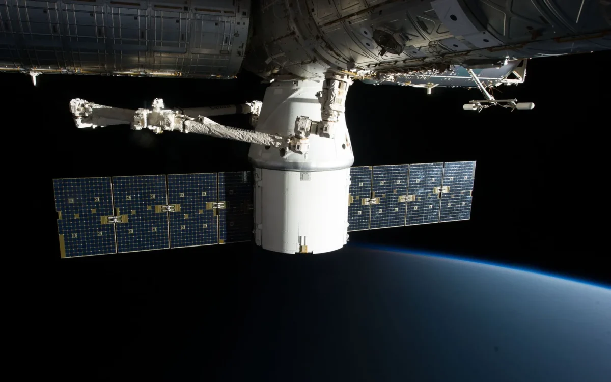 Capsulă spațială cu panouri solare și braț robotic lângă stația orbitală, deasupra Pământului