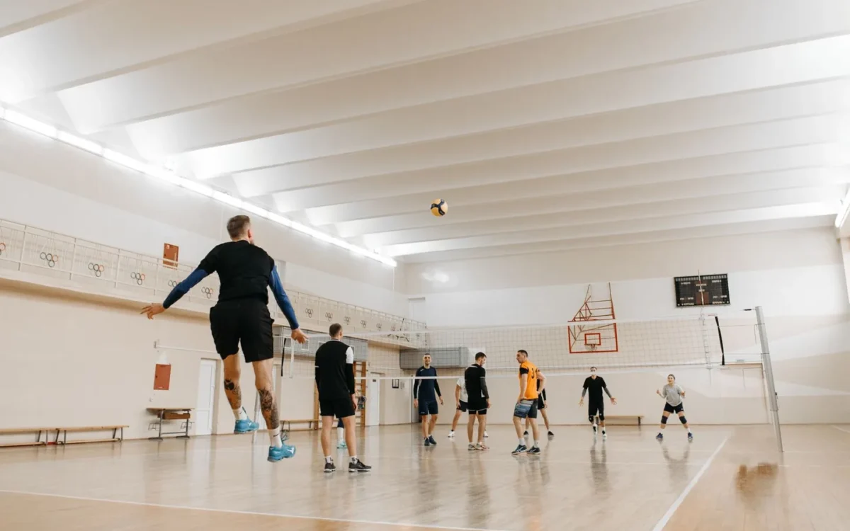 Jucători de volei și o minge deasupra fileului, într-o sală de sport