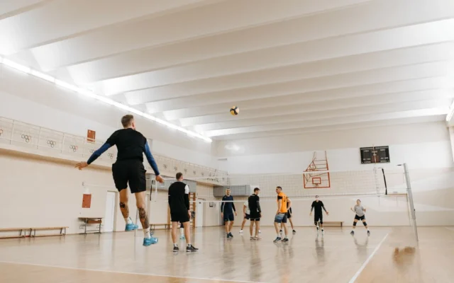 Jucători de volei și o minge deasupra fileului, într-o sală de sport