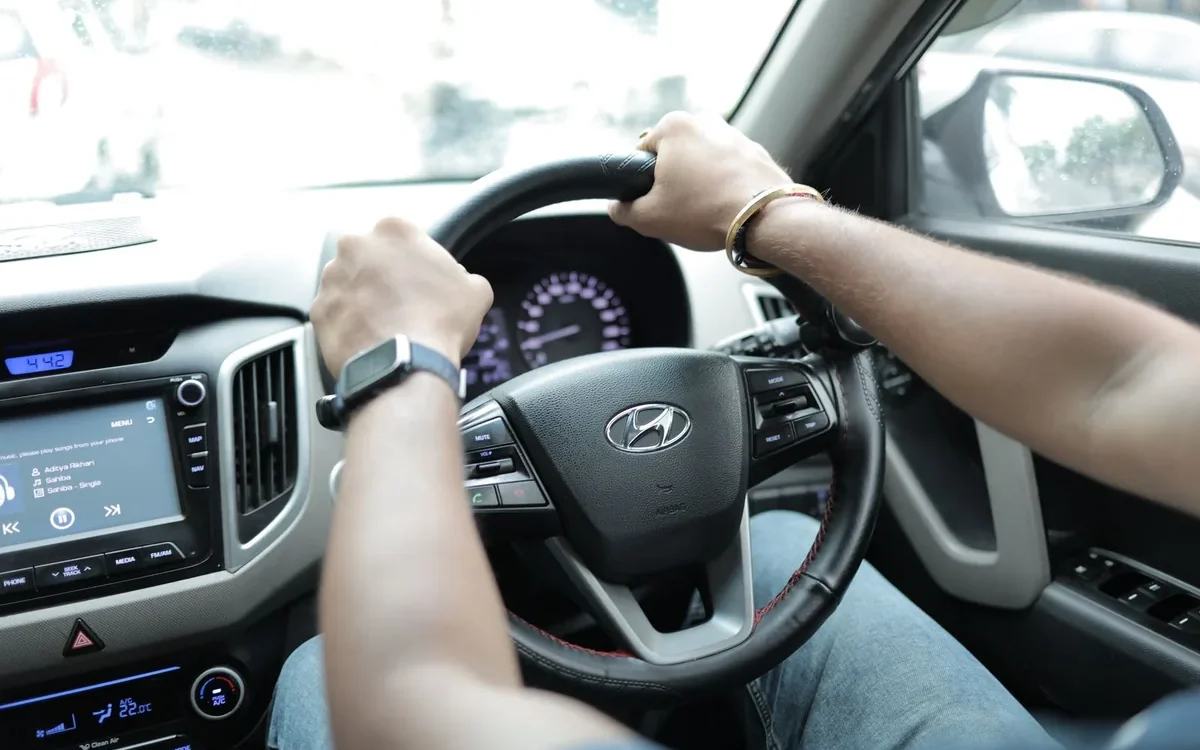 Mâinile unui șofer pe volan, lângă tabloul de bord al unui autoturism