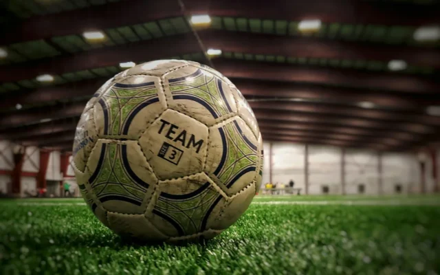 Minge de fotbal albă, cu model verde și negru, pe gazon într-o sală
