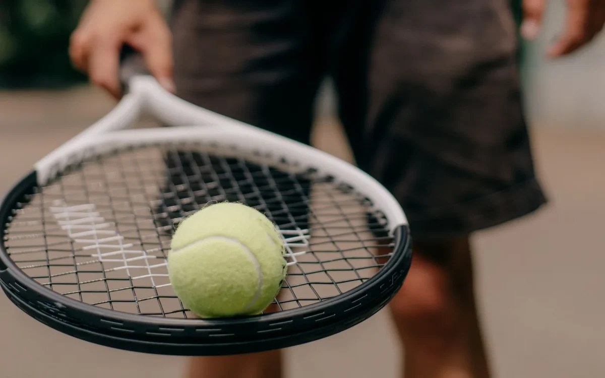 Minge galbenă pe racordajul unei rachete de tenis ținute de o persoană
