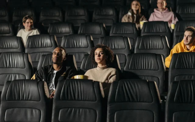Spectatori așezați pe rândurile de scaune ale unei săli de cinema.
