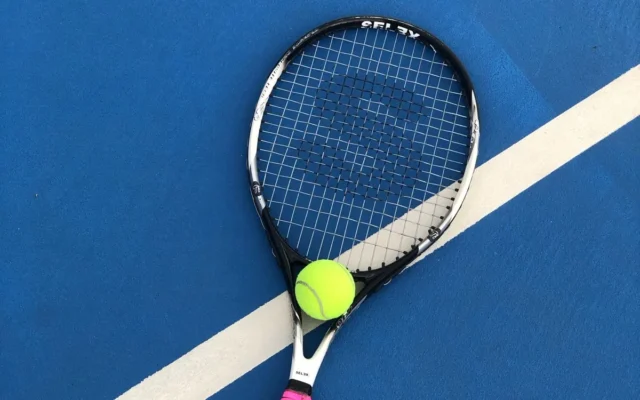Rachetă și minge de tenis pe suprafața albastră a unui teren, lângă o linie albă