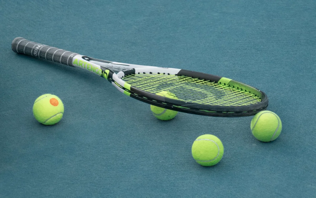 Rachetă și patru mingi de tenis pe suprafața albastră a unui teren