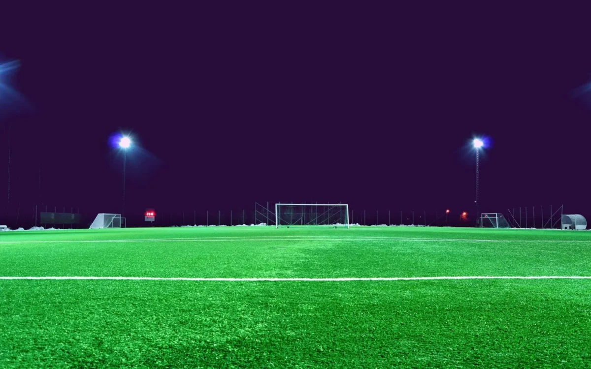Gazon și porți pe un teren de fotbal iluminat noaptea