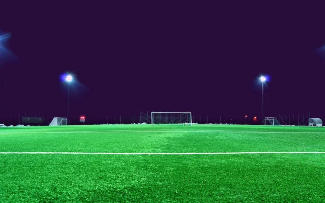 Gazon și porți pe un teren de fotbal iluminat noaptea