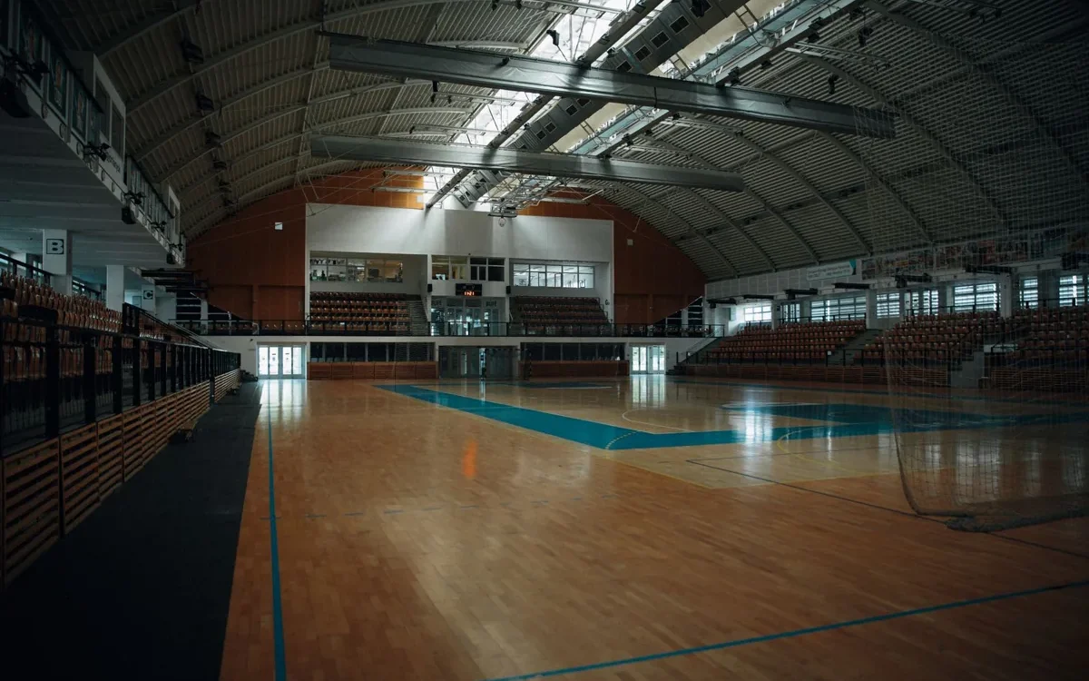 Teren de handbal acoperit cu parchet, porți și tribune goale într-o sală de sport